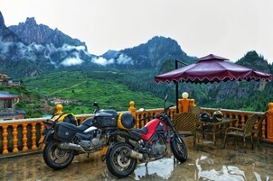Una motocicleta estacionada en una terraza mojada, con vistas a colinas verdes y una montaña al fondo.