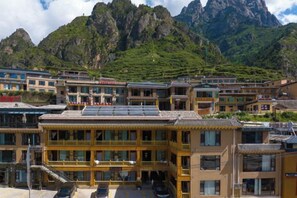 A traditional building with multiple balconies, a parking area, and a mountainous backdrop.