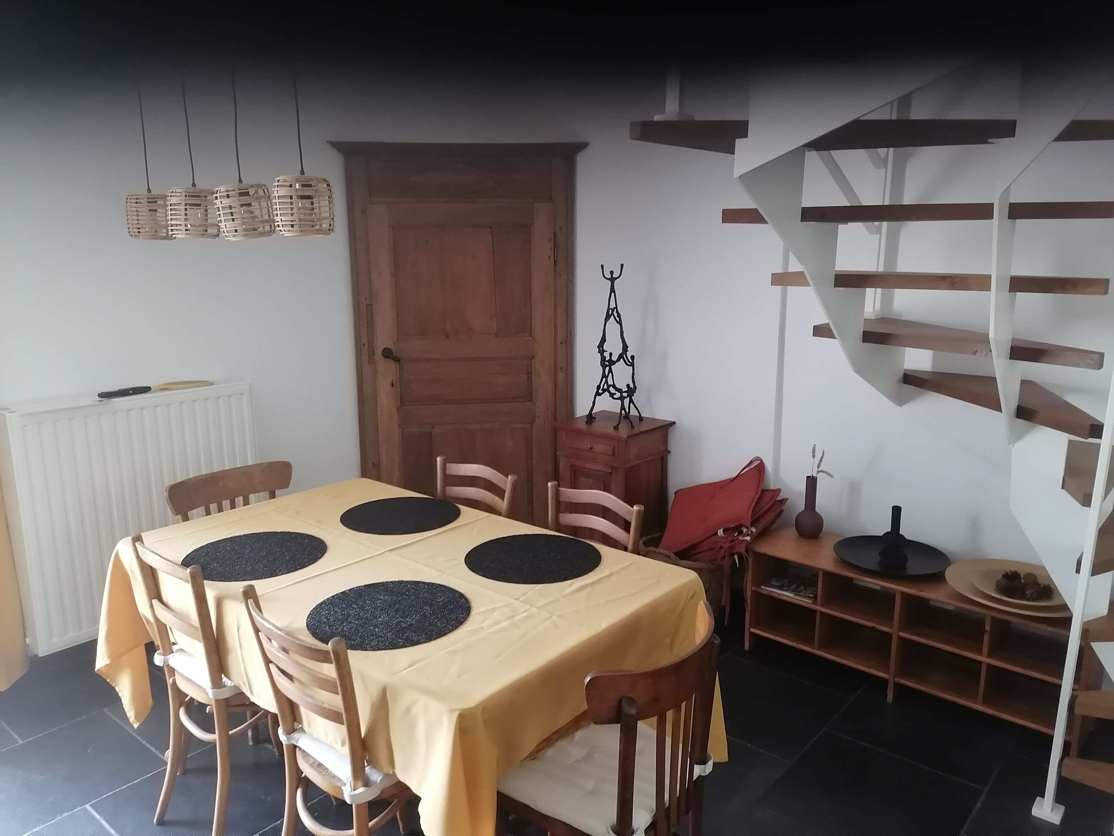 A dining area with a table set for six, wooden chairs, a wooden cabinet, a red bag, and a spiral staircase.