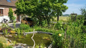 A garden with a pond, a car, and a house with a sloped roof. - Gîte de la Ferme du Semeur - Zaaiershof, Lessines. (Lessines)