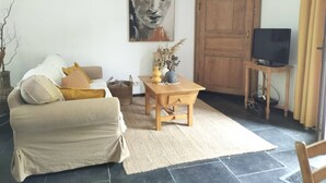 A living room with a sofa, a wooden table with a vase, a television on a stand, and a large wooden door. - Gîte de la Ferme du Semeur - Zaaiershof, Lessines. (Lessines)