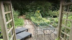 A garden patio with a glass table and metal chairs, surrounded by lush greenery and a wooden fence. - Gîte de la Ferme du Semeur - Zaaiershof, Lessines. (Lessines)