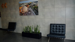 A modern lobby with a large cityscape painting, two black chairs, and a black planter with green plants. - Welcome to Ruelle505 (Tijuana)