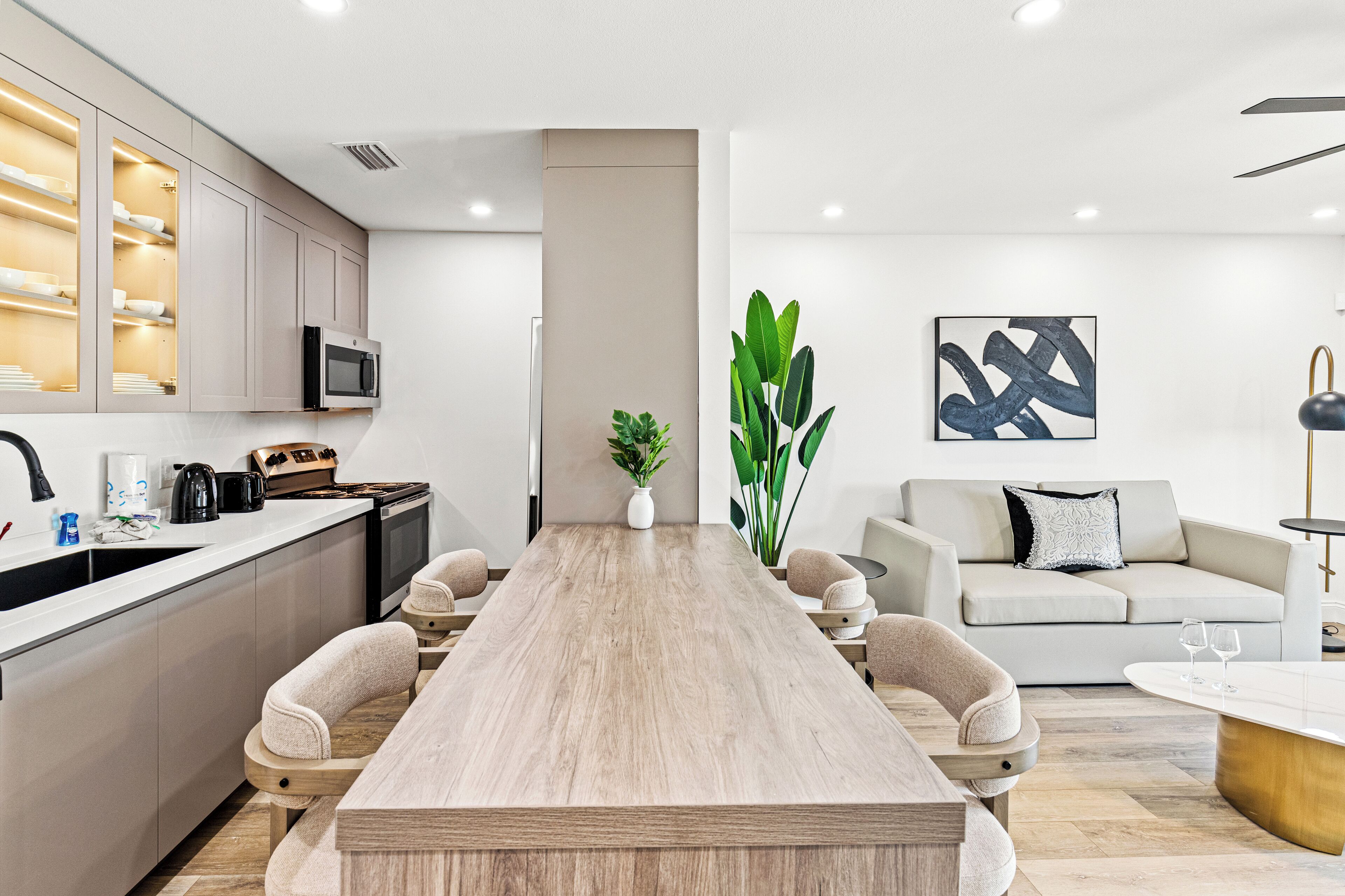 A modern kitchen with a long wooden table, built-in appliances, and a dining area with a sofa and chairs.