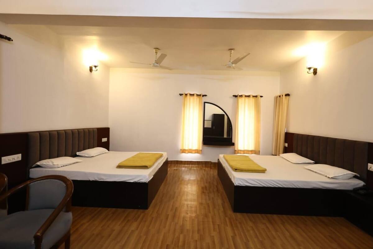 A hotel room with two single beds, wooden flooring, ceiling fans, and a mirror above the beds.