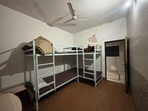 A bunk bed room with a ceiling fan, a door, and a wall with a textured pattern. - Hotel Moksha (Rishikesh)