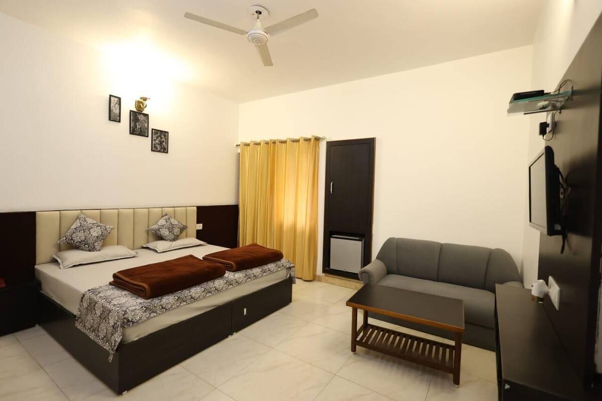 A modern hotel room with a bed, a sofa, a coffee table, and a TV mounted on the wall.