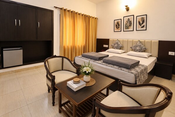 A hotel room with a bed, two bedside tables, a desk with chairs, a small kitchenette, and a bathroom. - Hotel Moksha (Rishikesh)