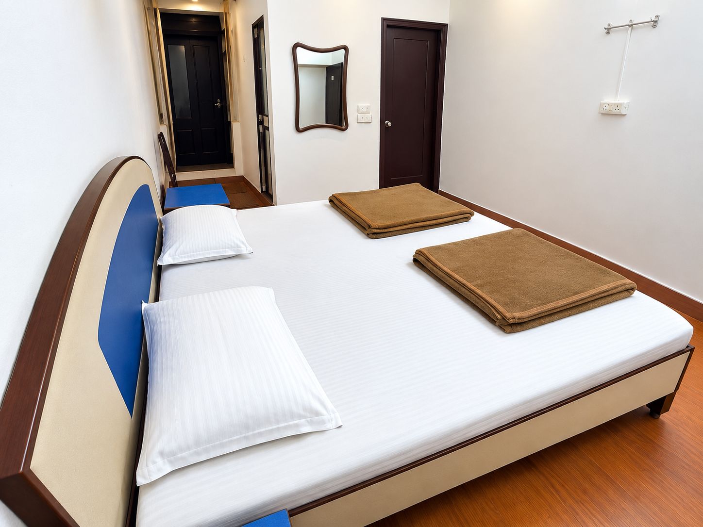 A neatly made bed with pillows and a folded blanket, a bedside table, a mirror, and a door in a hotel room.