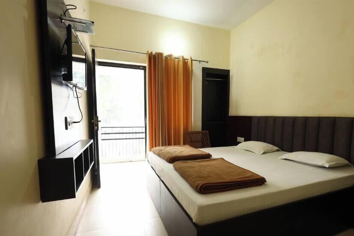 A hotel room with a bed, a chair, a TV, and a window with curtains.