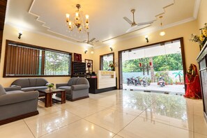 A reception area with a reception desk, seating, a chandelier, ceiling fans, and a view of the outside. - Hotel Moksha (Rishikesh)