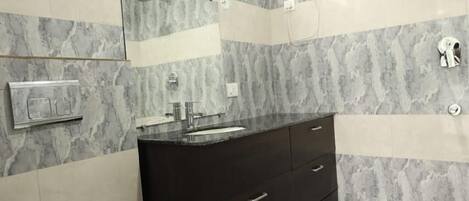 Un baño con inodoro blanco, tocador negro, espejo y toallero.