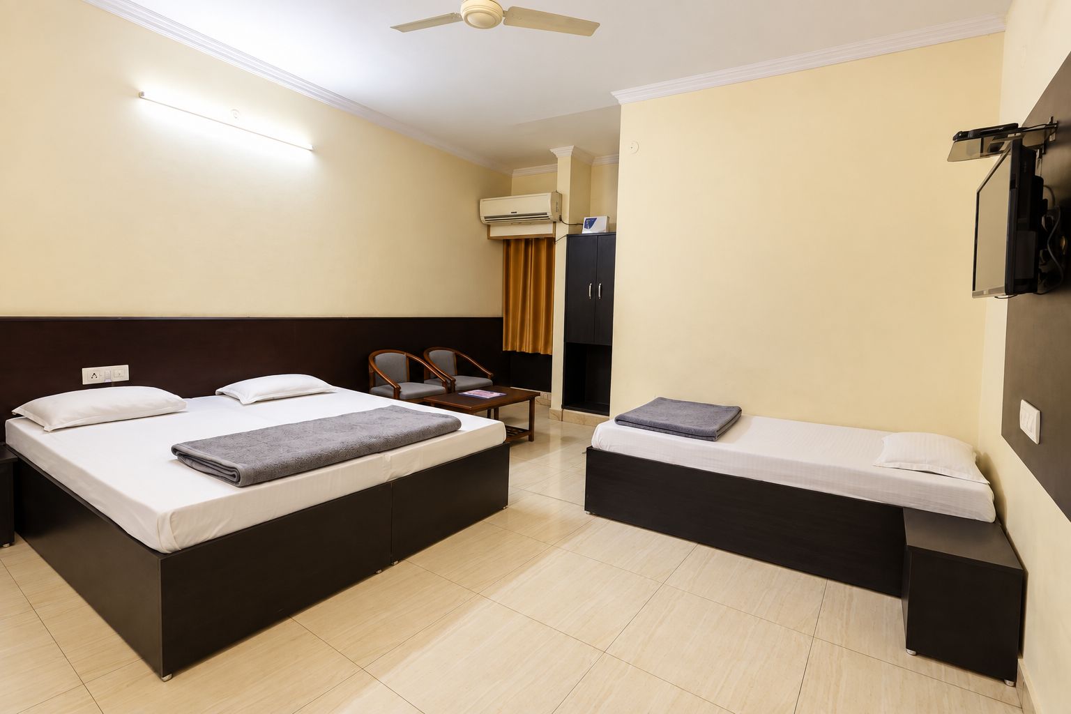 A hotel room with two beds, a desk, a chair, an air conditioning unit, and a ceiling fan.