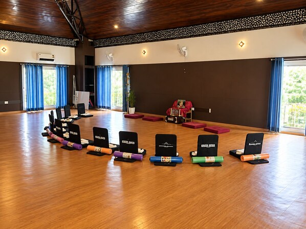 A spacious room with a wooden floor, arranged seating, and a decorative wall. - Hotel Moksha (Rishikesh)