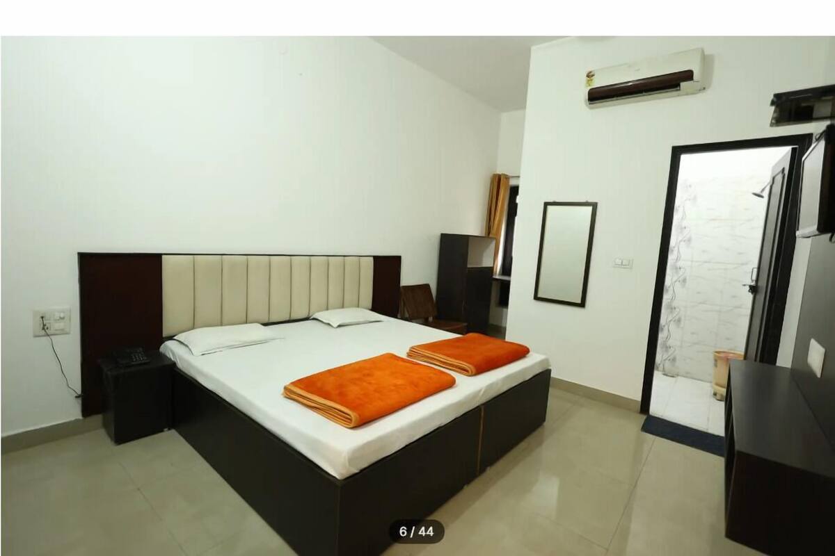 A hotel room with a bed, bedside table, and an air conditioning unit.