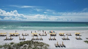 Ein Strand mit Liegestühlen und Sonnenschirmen, einem klaren Himmel und dem Meer.