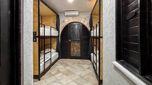 A narrow hallway with bunk beds labeled 1 and 2, a tiled floor, and a stone archway at the end. - Hostal CASA MX quinta avenida (Playa del Carmen)