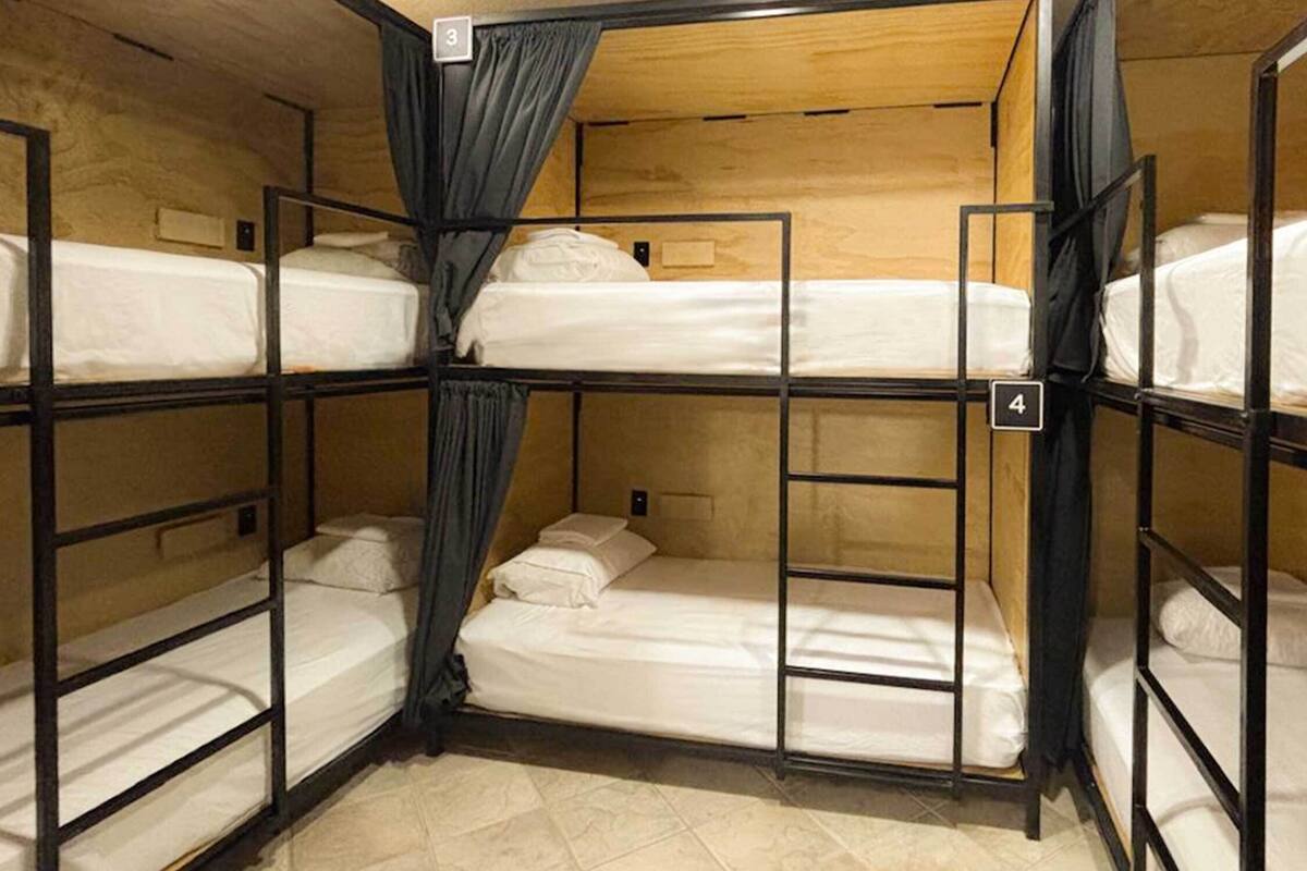 Camera con letti a castello, pareti in legno e ringhiere in metallo. Sono presenti due letti a castello, ciascuno con materasso e cuscini. Una scala è fissata al lato del letto inferiore.