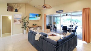 Ein Wohnzimmer mit einem dunkelblauen Sofa, einem Flachbildfernseher und einem Deckenventilator.