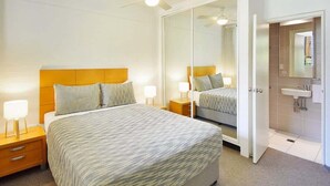 Quarto de hotel com uma cama grande, mesas de cabeceira, um espelho e um banheiro com pia e espelho.