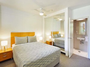 Een hotelkamer met een groot bed, nachtkastjes, een spiegel en een badkamer met een wastafel en spiegel.