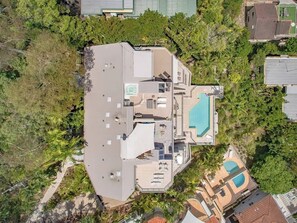 Um imóvel residencial com piscina no terraço, várias varandas e vegetação exuberante ao redor.