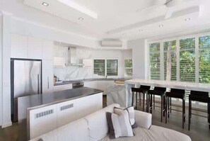 A modern kitchen with a central island, a dining area with bar stools, and a large window providing a view of greenery.