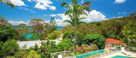 Zona de piscina con vistas despejadas al océano, rodeada de exuberante vegetación y un cielo despejado.