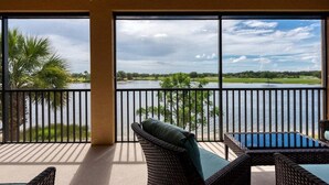 A balcony with wicker furniture, a ceiling fan, and a view of a lake and greenery. - Impeccable 3 BR / 2 BA home with expansive lake view - Serenity Garden (Venice)