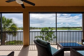 Un balcon doté de meubles en osier, d’un ventilateur de plafond et offrant une vue sur un lac et la verdure environnante.