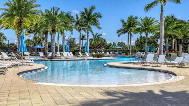 A pool area with lounge chairs and umbrellas, surrounded by palm trees. - Impeccable 3 BR / 2 BA home with expansive lake view - Serenity Garden (Venice)