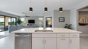 A modern kitchen with a central island, white cabinetry, and pendant lighting. - Impeccable 3 BR / 2 BA home with expansive lake view - Serenity Garden (Venice)