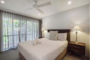 A hotel room with a bed, two bedside lamps, a ceiling fan, and a window with curtains.