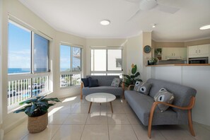 A modern living room with a grey sofa, a round coffee table, and a view of the sea through large windows.