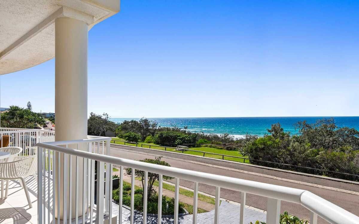 Un balcon avec vue sur la mer, une route et la verdure.