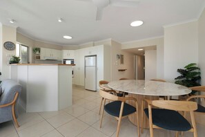 Cozinha moderna com armários brancos, ilha central e área de refeições com mesa redonda e cadeiras.