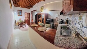 Uma cozinha com teto de madeira, uma área de refeições com mesa e cadeiras, e uma bancada com pia e azulejos decorativos.