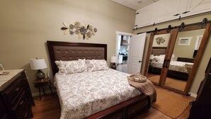 A bedroom with a large bed, wooden headboard, a bedside table with a lamp, a dresser, a mirror, and a sliding door closet. - Charming 1-bedroom apartment with WiFi, AC in downtown Kalispell Main Street (Kalispell)