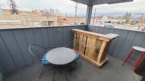 A covered outdoor patio with a round table and chairs, a wooden bar, and a red stool. - Charming 1-bedroom apartment with WiFi, AC in downtown Kalispell Main Street (Kalispell)