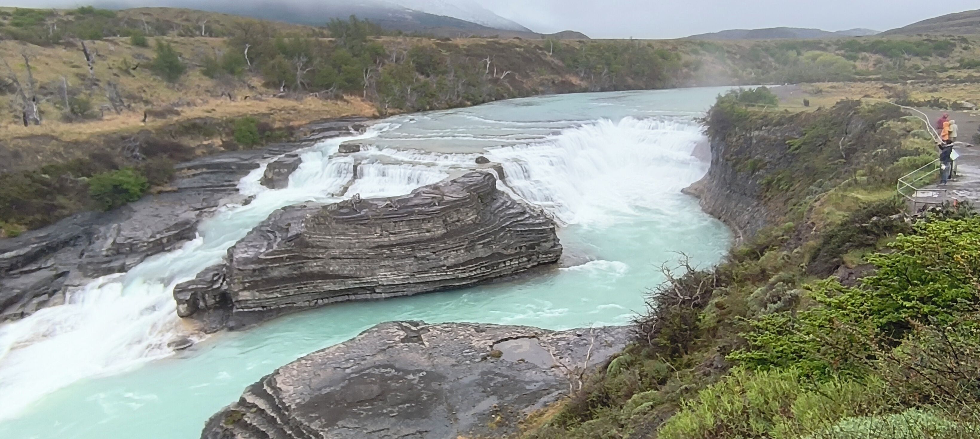 A waterfall cascading over a rocky riverbed with a person standing on a viewing platform.
