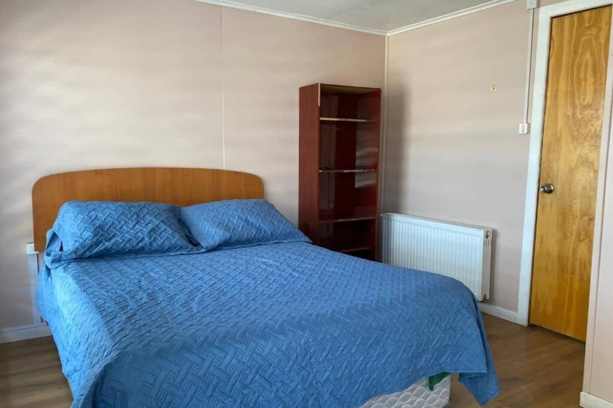 Une chambre à coucher avec un lit en bois, une couvre-lit matelassée bleue, une armoire en bois et un radiateur.