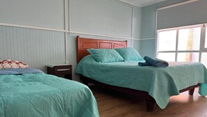 A room with two beds, wooden headboards, and a large window.