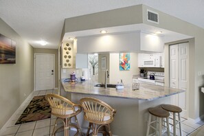 A kitchen with a central island, two bar stools, a microwave, and a sink.