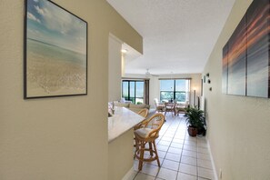 A spacious kitchen with a marble countertop, wicker chairs, and large windows.