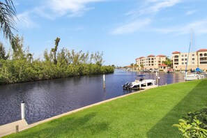 A canal with boats docked, a grassy bank, and a row of buildings with red roofs. - Gorgeous 2 BR / 2 BA waterfront condo in Punta Gorda - The River's End (Punta Gorda)