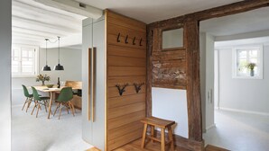 Una stanza con pavimento in legno, zona pranzo con sedie verdi, parete in legno con uno specchio e un piccolo sgabello di legno.