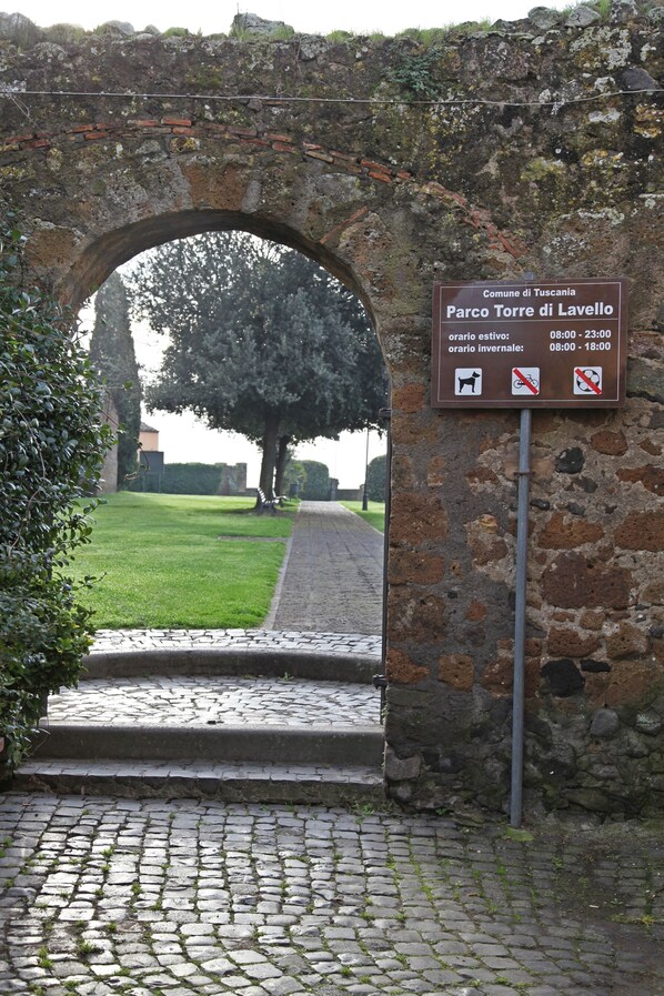 Un antiguo arco de piedra que da acceso a una zona verde con un cartel que indica 'Parco Torre di Lavello' y horarios de estacionamiento.