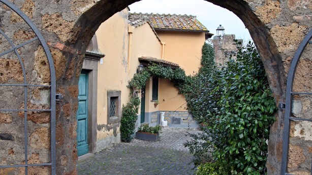 A cobblestone alleyway leading to a rustic building with a green door and a stone archway. - Nives Holiday House, home in the ancient castle walls in the historic center. (Tuscania)