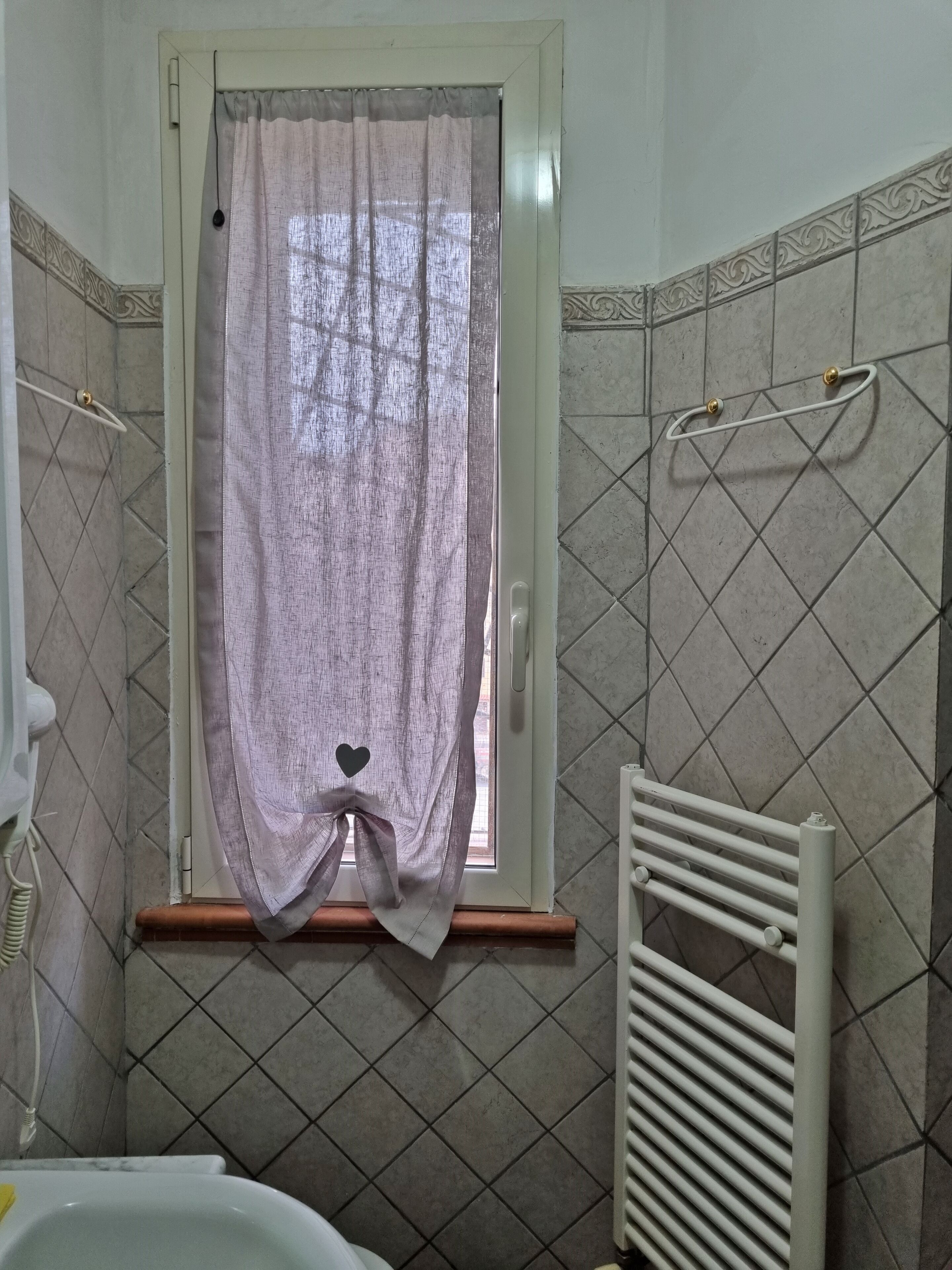 Un bany amb finestra, parets revestides de rajola, un escurapulides i un radiador.