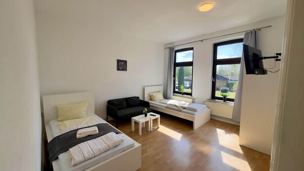 Ein modernes Schlafzimmer mit einem Bett, einem schwarzen Sofa, einem kleinen Tisch und einem Fenster mit Blick nach draußen.